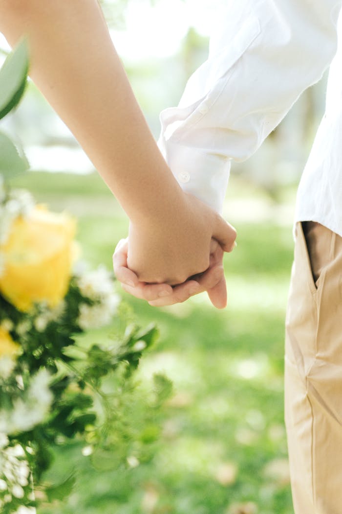 Tender moment of a couple holding hands amidst a lush garden setting.